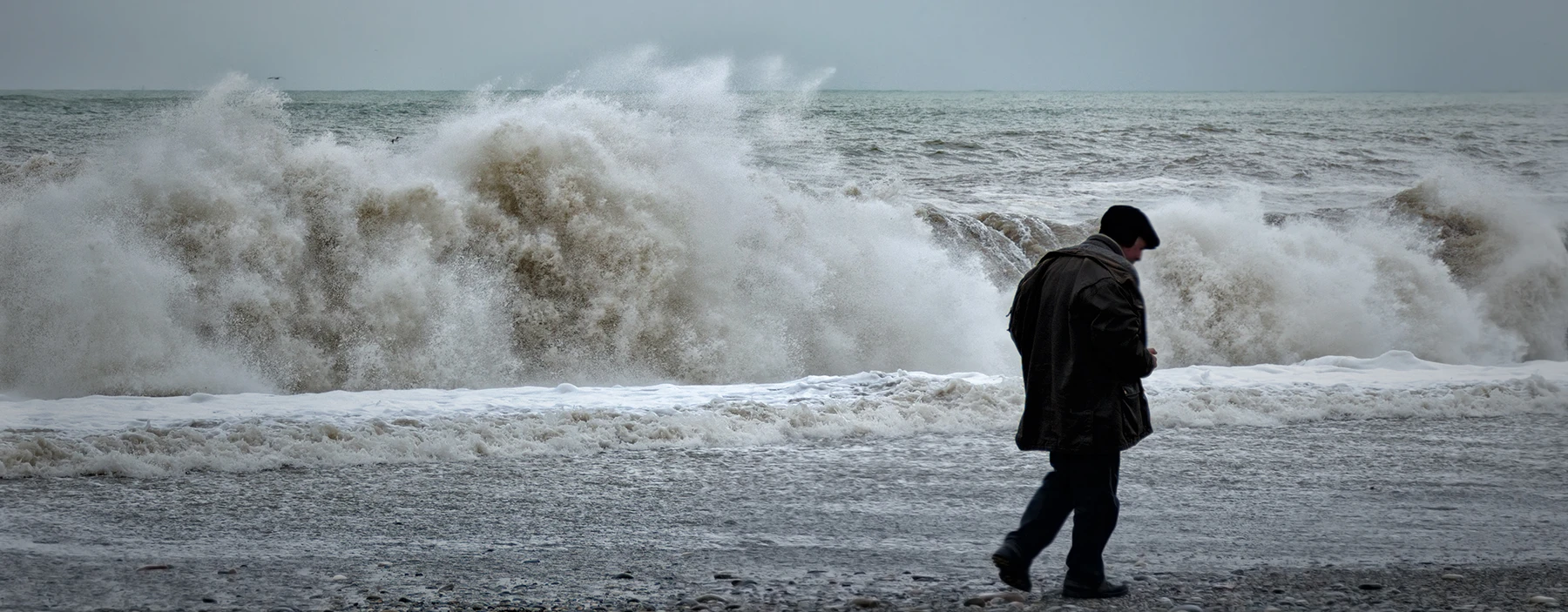 person walking on a beach with large wave crashing